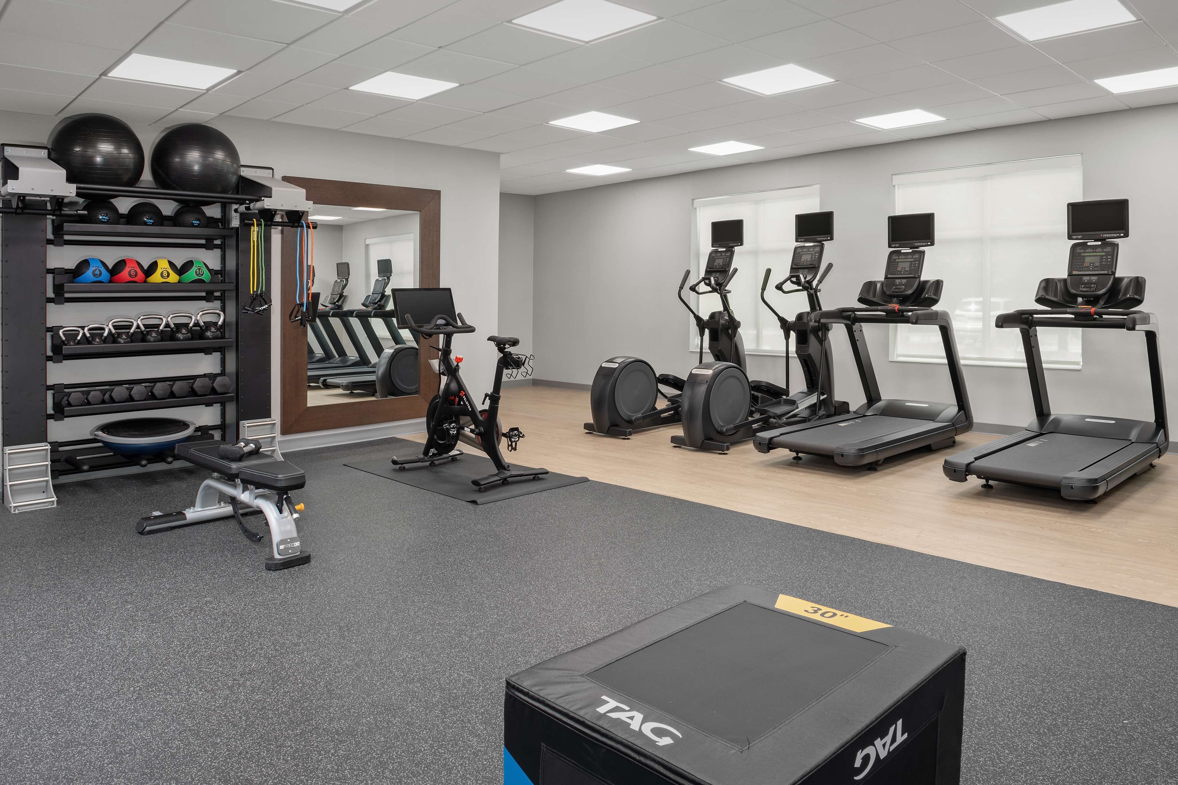 Une salle de sport équipée de tapis de course, de vélos elliptiques et d’une variété d’haltères et de ballons d’exercice.