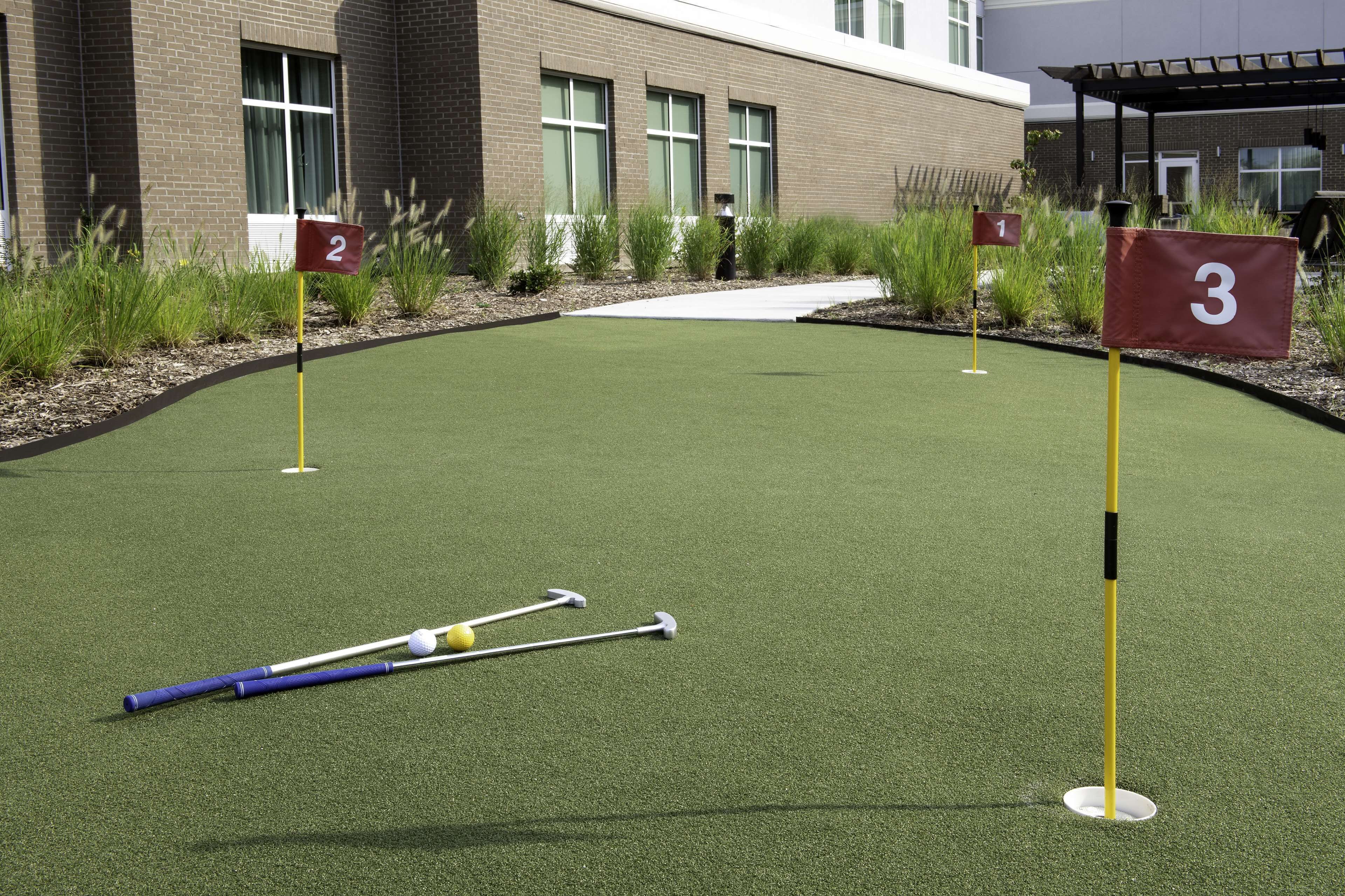 Un parcours de minigolf avec des trous numérotés, un revêtement de sol synthétique et un bâtiment en arrière-plan.