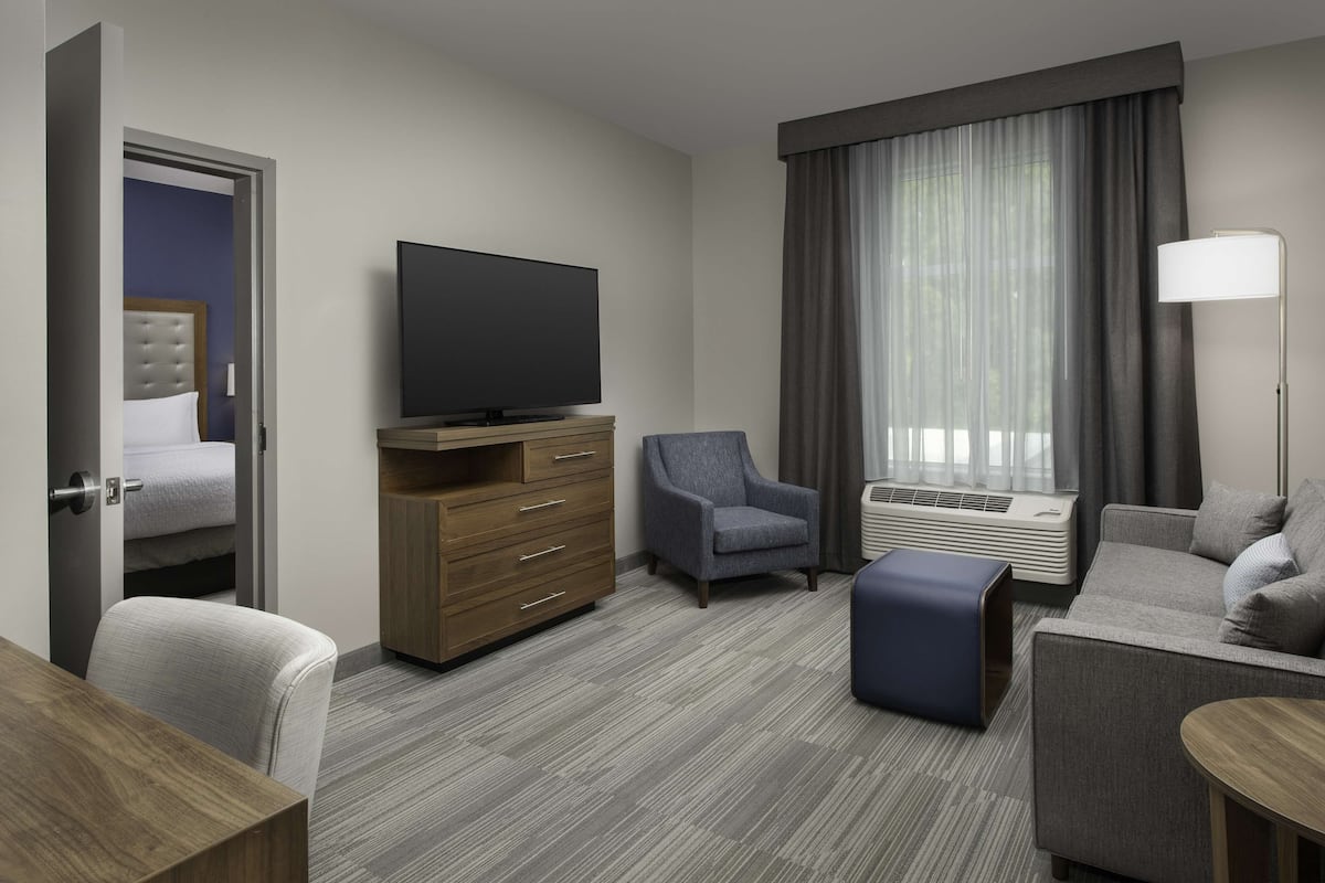 Une chambre d’hôtel équipée d’un lit, d’une télévision, d’un canapé, d’un fauteuil, d’un bureau et d’une fenêtre avec des rideaux.