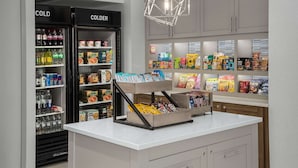 Una tienda de suites con dispensadores refrigerados de bebidas, estantes con aperitivos y una lámpara colgante moderna.