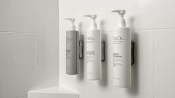 A bathroom with white tiles and three white bottles of shampoo and conditioner on a wall-mounted shelf.