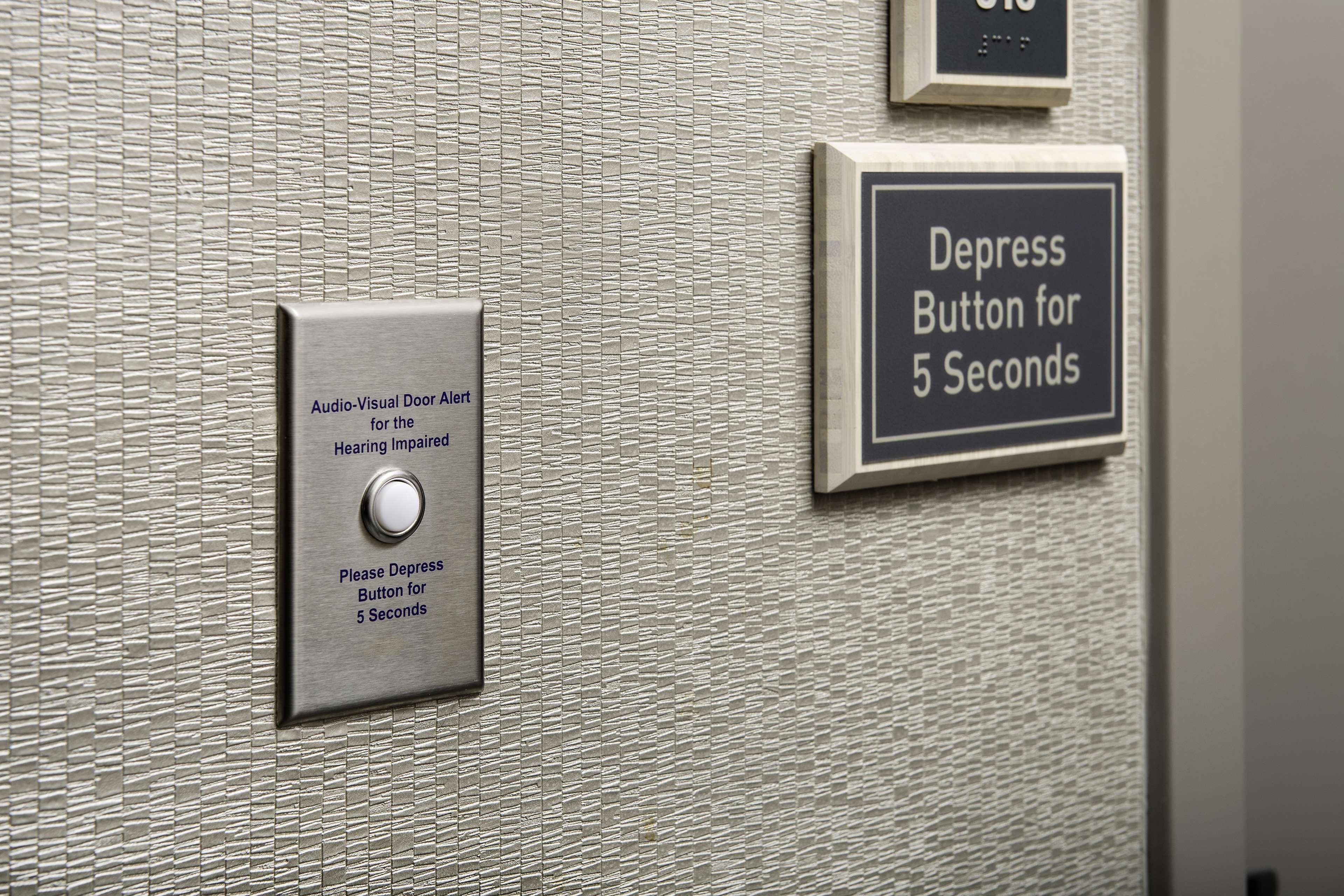 A wall-mounted depression button for 5 seconds and an audio-visual door alert for the hearing impaired.