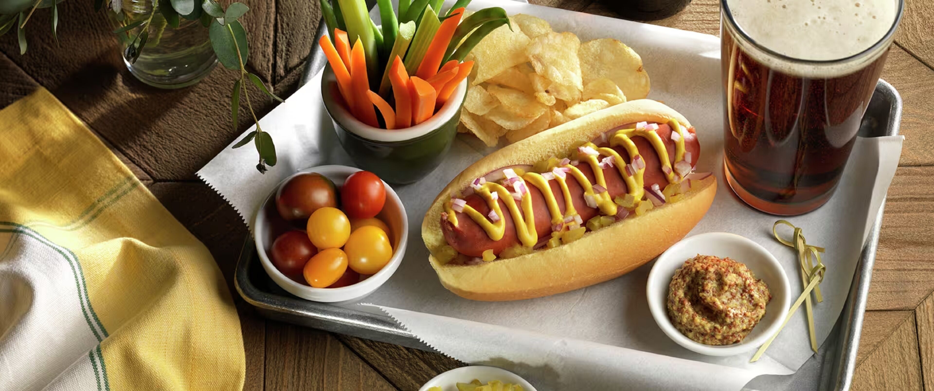 A meal tray with a hot dog, chips, cherry tomatoes, and a drink.