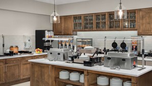 Una cocina moderna con armarios de madera, una isla central con platos, una cafetera y máquinas para hacer gofres.