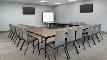 A conference room with a long table, multiple chairs, a whiteboard, and a flat-screen TV on the wall.