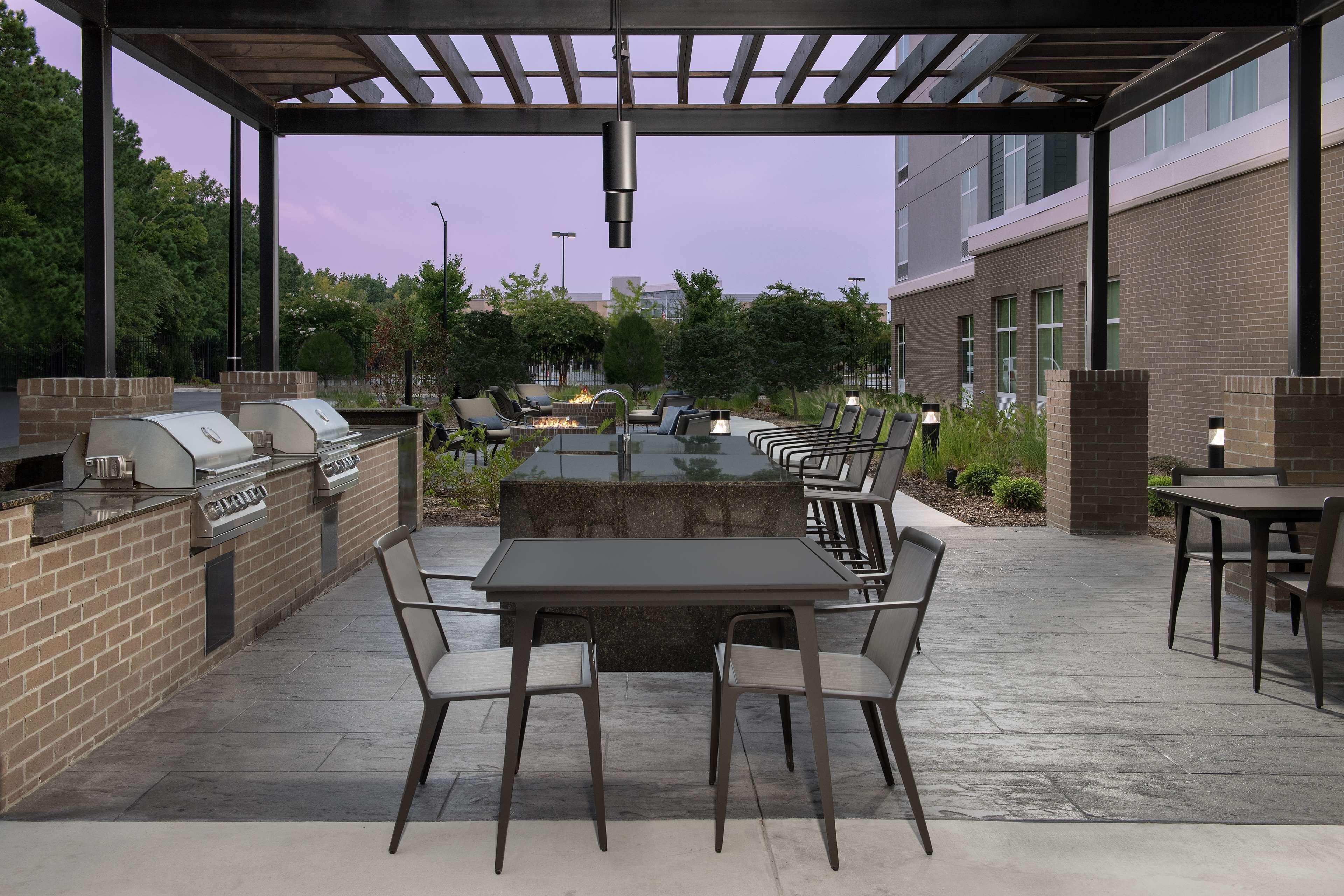 Un patio exterior con una barbacoa de ladrillo, una mesa con cubierta de vidrio y sillas.