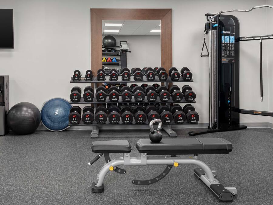 Ett gym med en bänkpress, kettlebells, hantlar och en kabelmaskin.