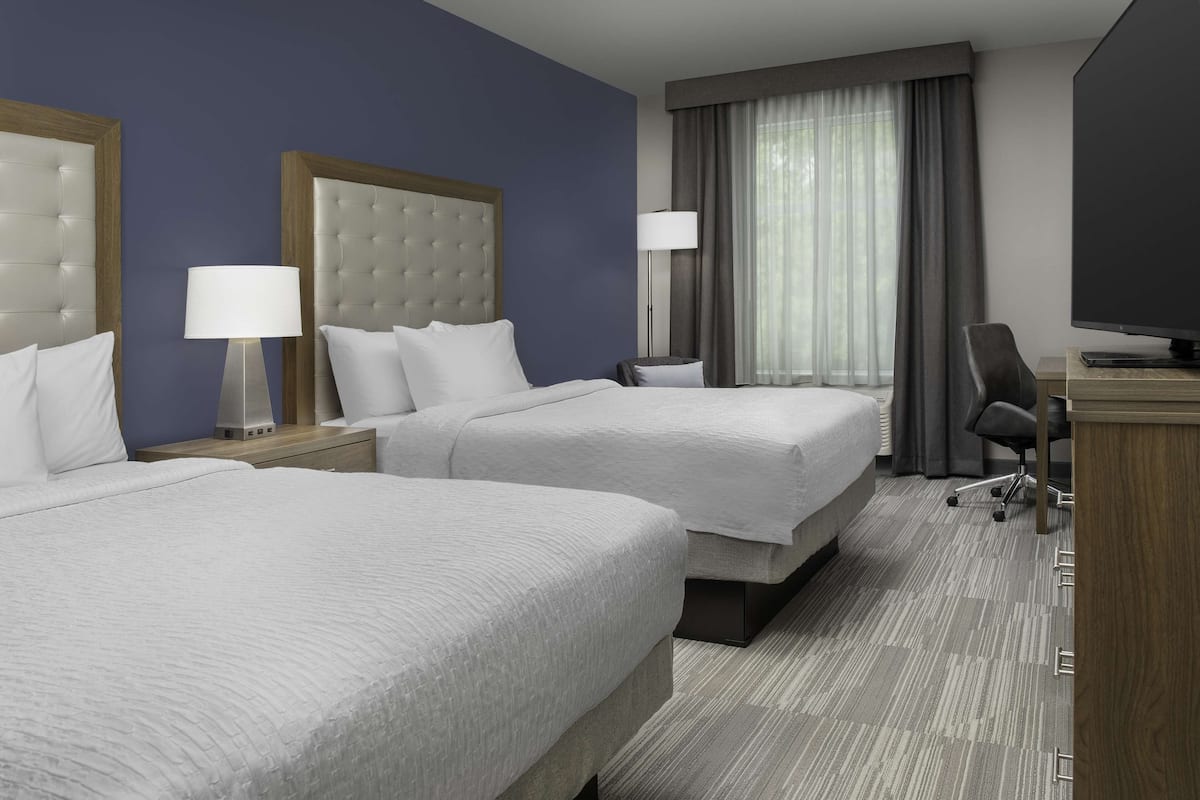 Une chambre d’hôtel avec deux lits, un bureau, une chaise et une télévision.