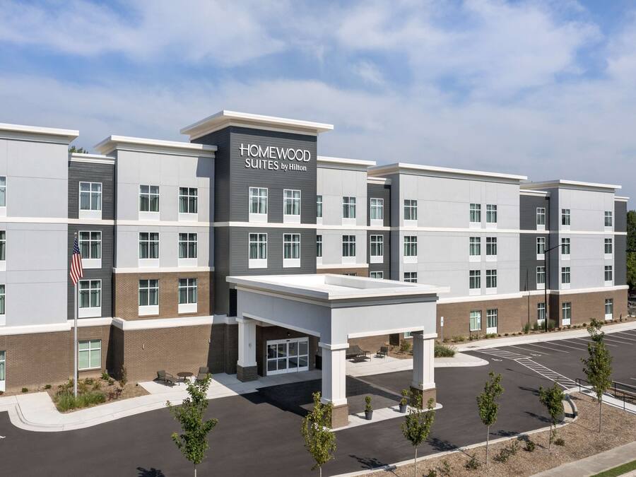 A multi-story hotel with a modern design, featuring a prominent entrance with a covered waiting area and a parking lot.