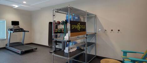 A gym with a treadmill, a spin cycle station, and a blue chair.