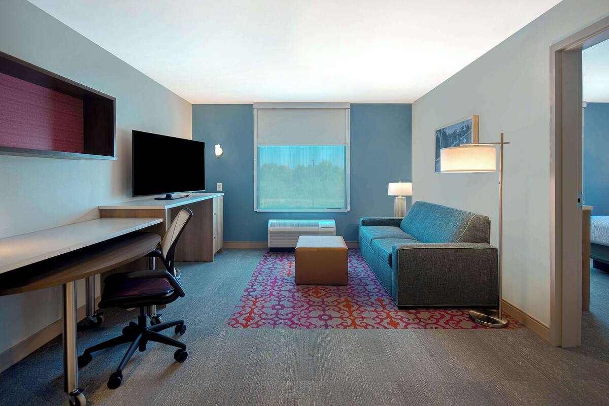 Ein Hotelzimmer mit Schreibtisch, Stuhl, Fernseher, Sofa und einem Fenster mit Blick.