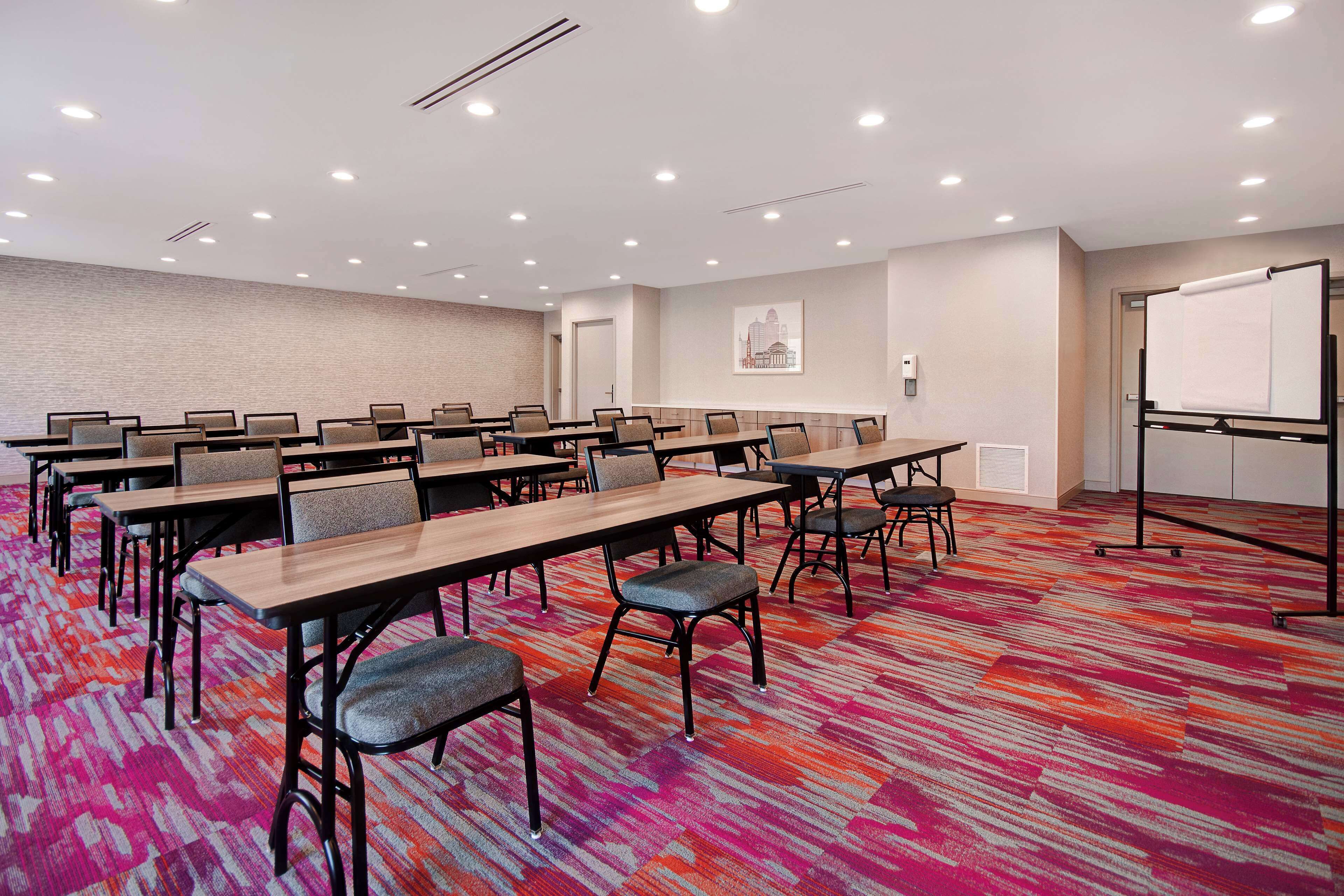 A conference room with multiple tables and chairs, a carpeted floor, and a whiteboard on the right.