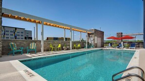 A swimming pool with a wooden pergola, green and yellow chairs, and red umbrellas. - Home2 Suites By Hilton Shepherdsville Louisville South (Louisville)