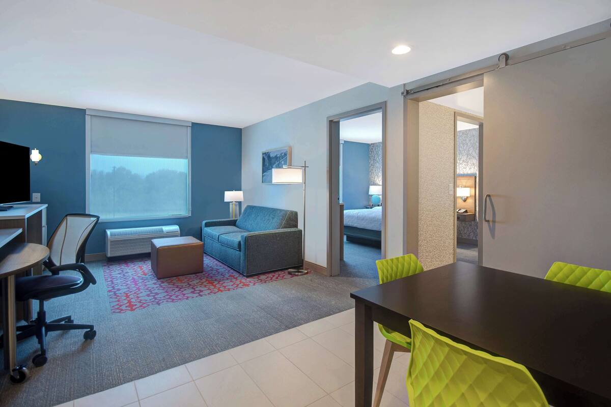 Ein modernes Hotelzimmer mit Schreibtisch, Stuhl, Sofa und Esstisch mit Stühlen.