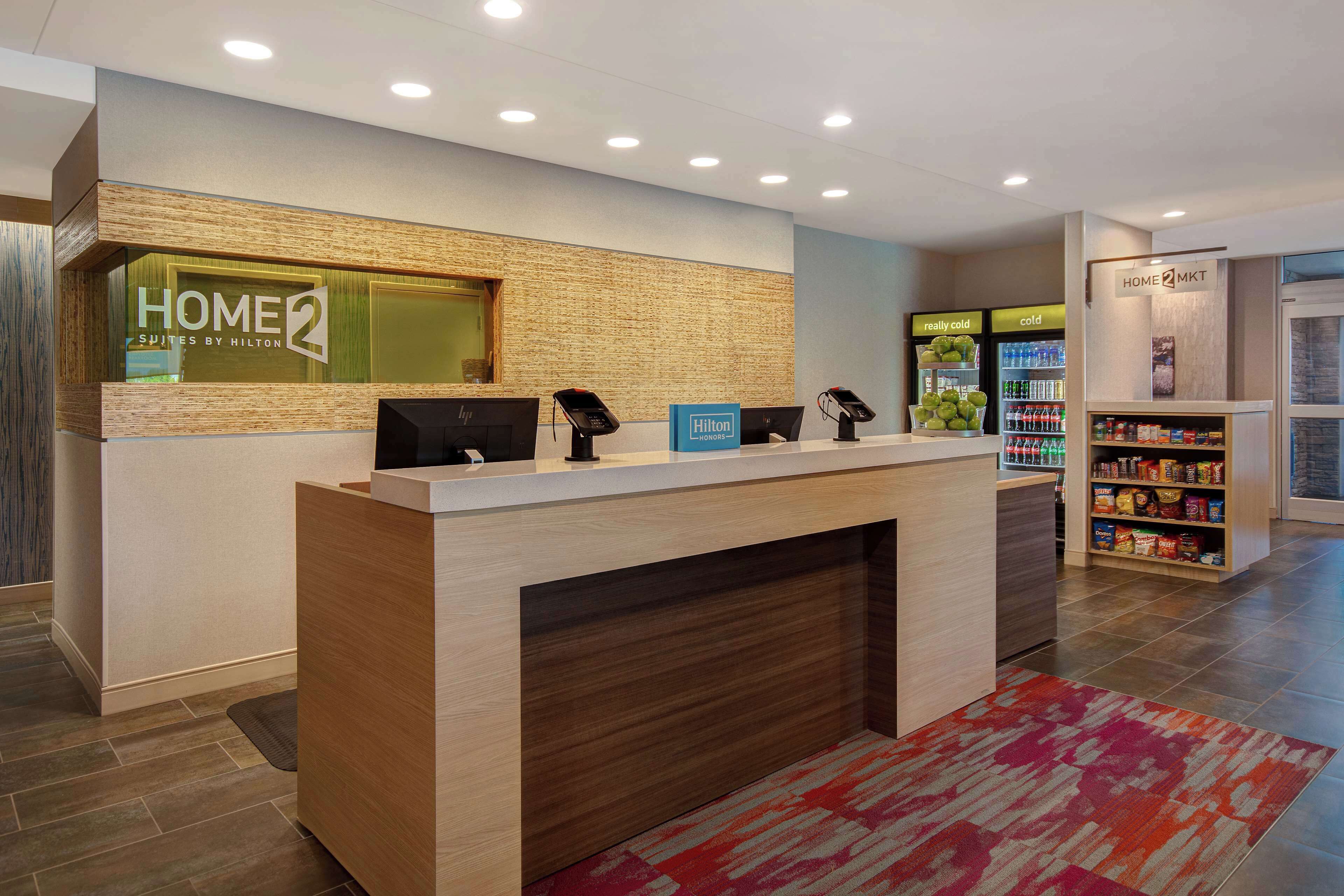A hotel reception desk with a wooden counter, a digital screen, and a sign for 'HOME2 SPITES BY HILTON'.