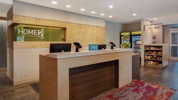 A hotel reception desk with a wooden counter, a digital screen, and a sign for 'HOME2 SPITES BY HILTON'.