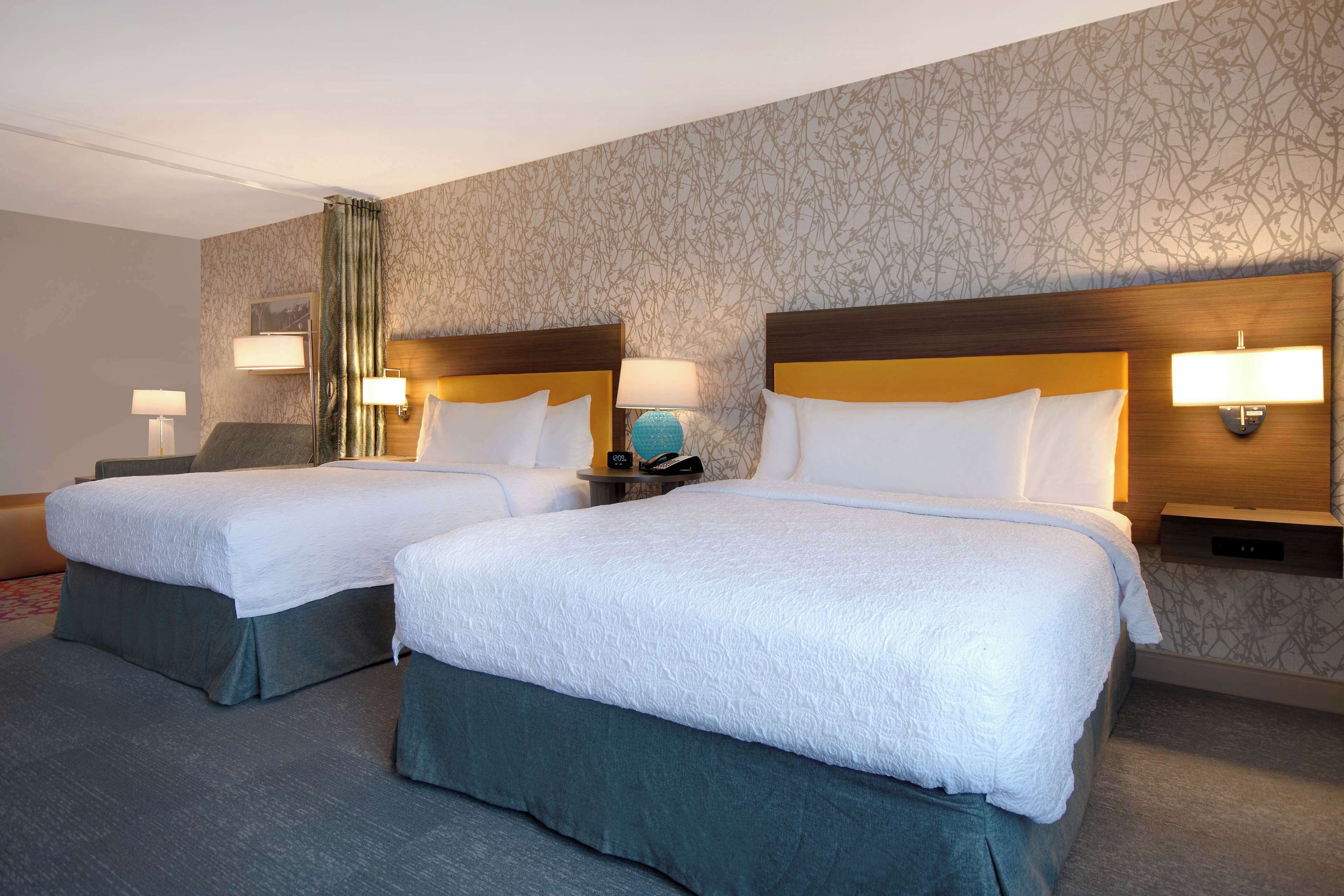 Een hotelkamer met twee bedden, elk met een houten hoofdeinde, witte lakens en bedlampjes.