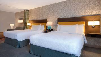 A hotel room with two beds, each with a wooden headboard, white linens, and bedside lamps.