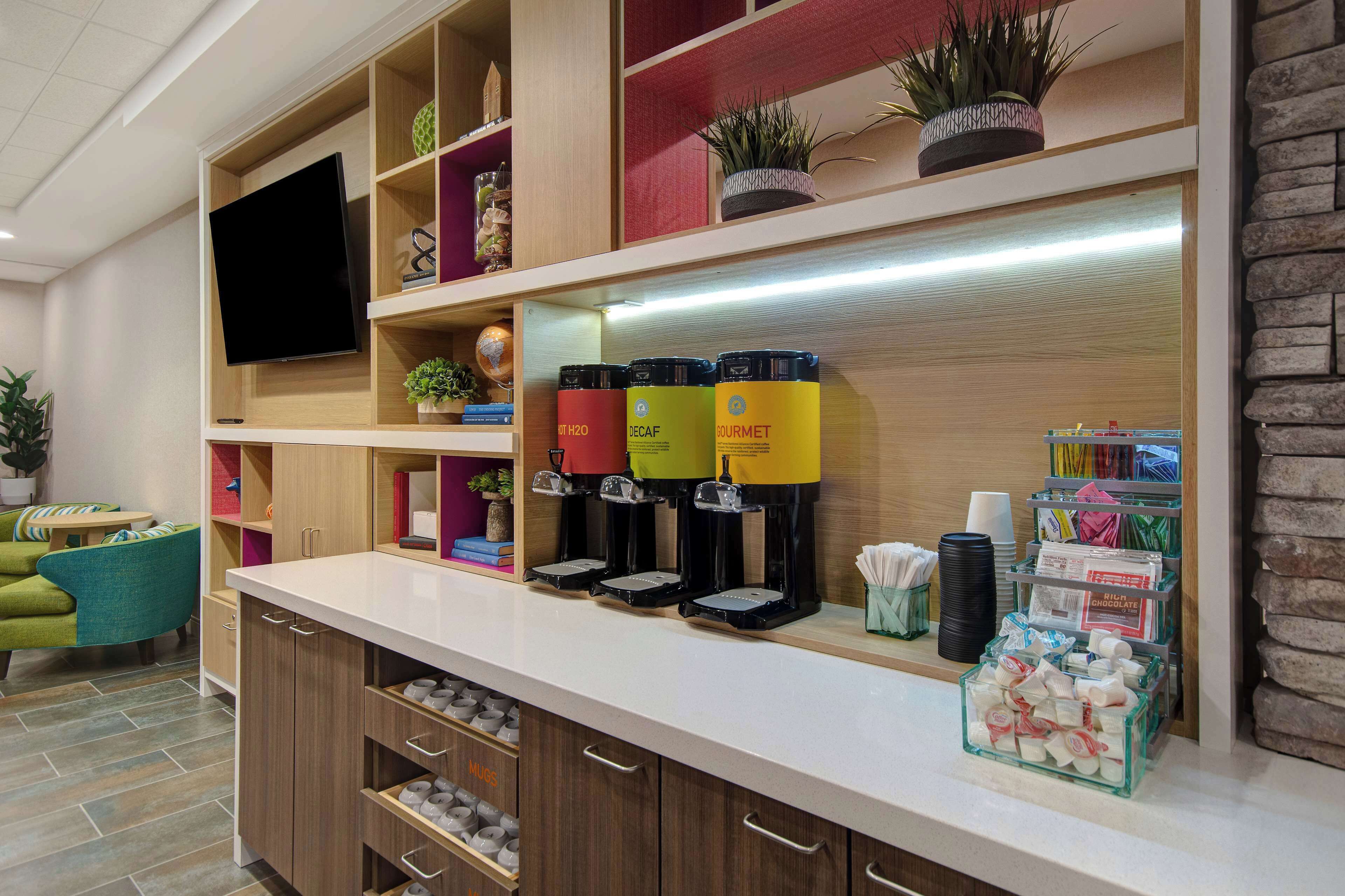 A hotel reception area with a coffee station, shelves with various items, and a television.