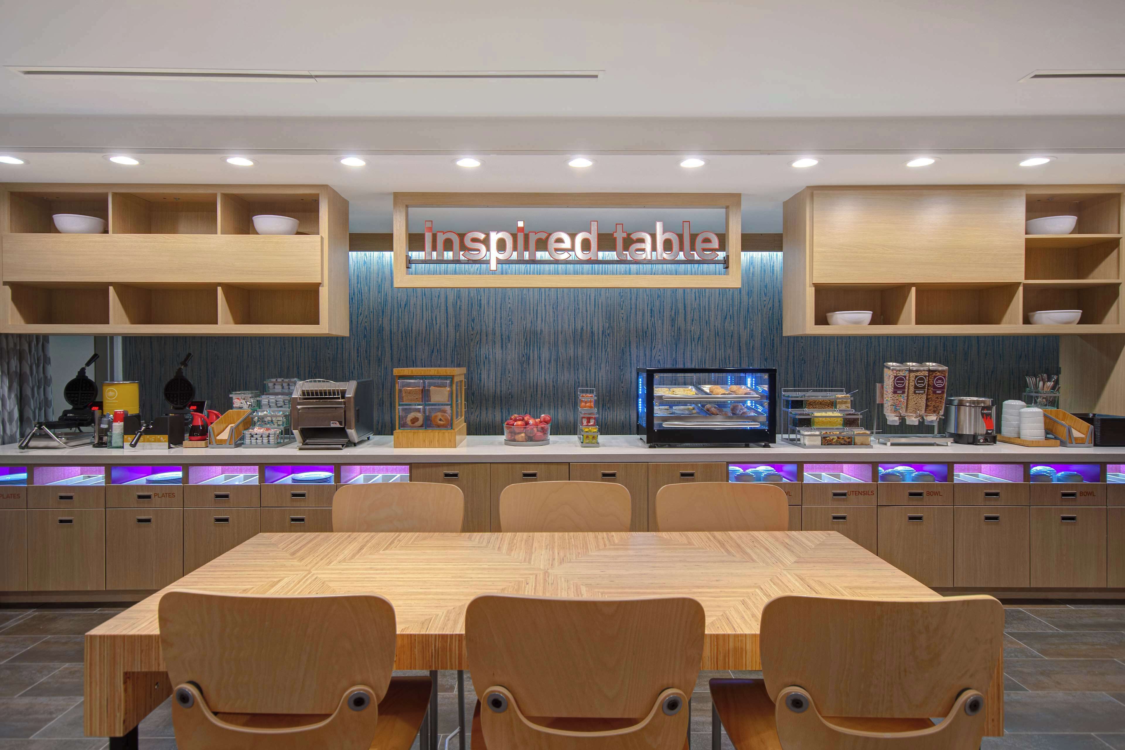 A restaurant with a wooden table and chairs, a counter with food items, and a sign that reads "inspired table".