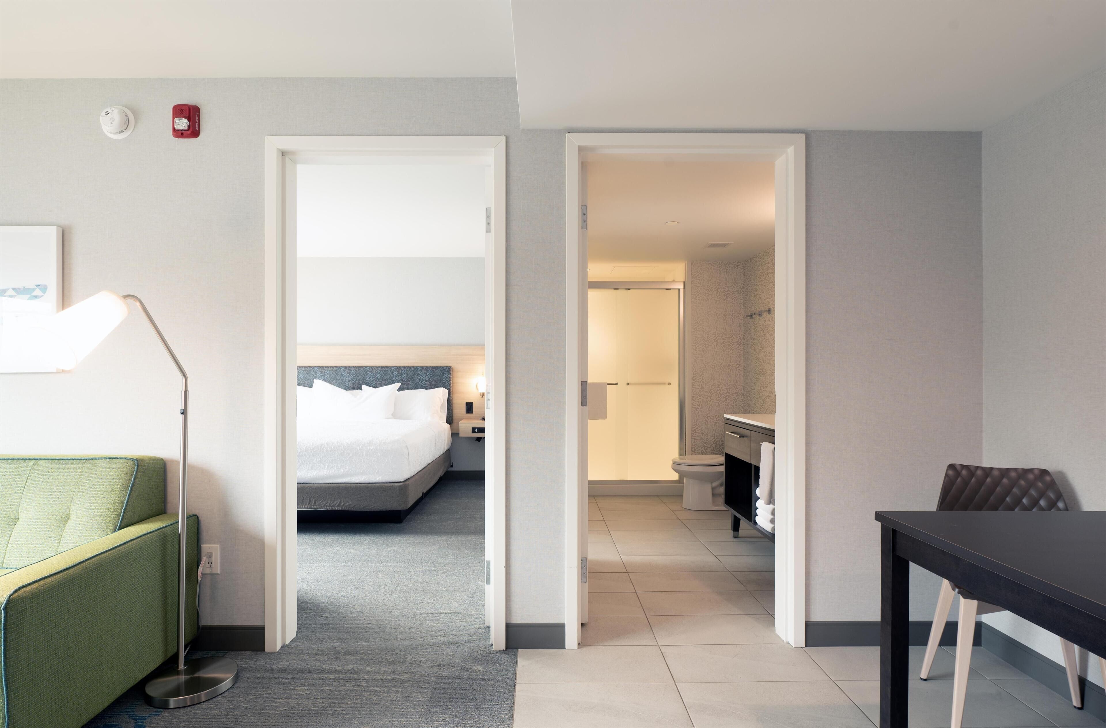 Une chambre d’hôtel avec un lit, un canapé vert, une table et une salle de bain visible à travers une porte ouverte.