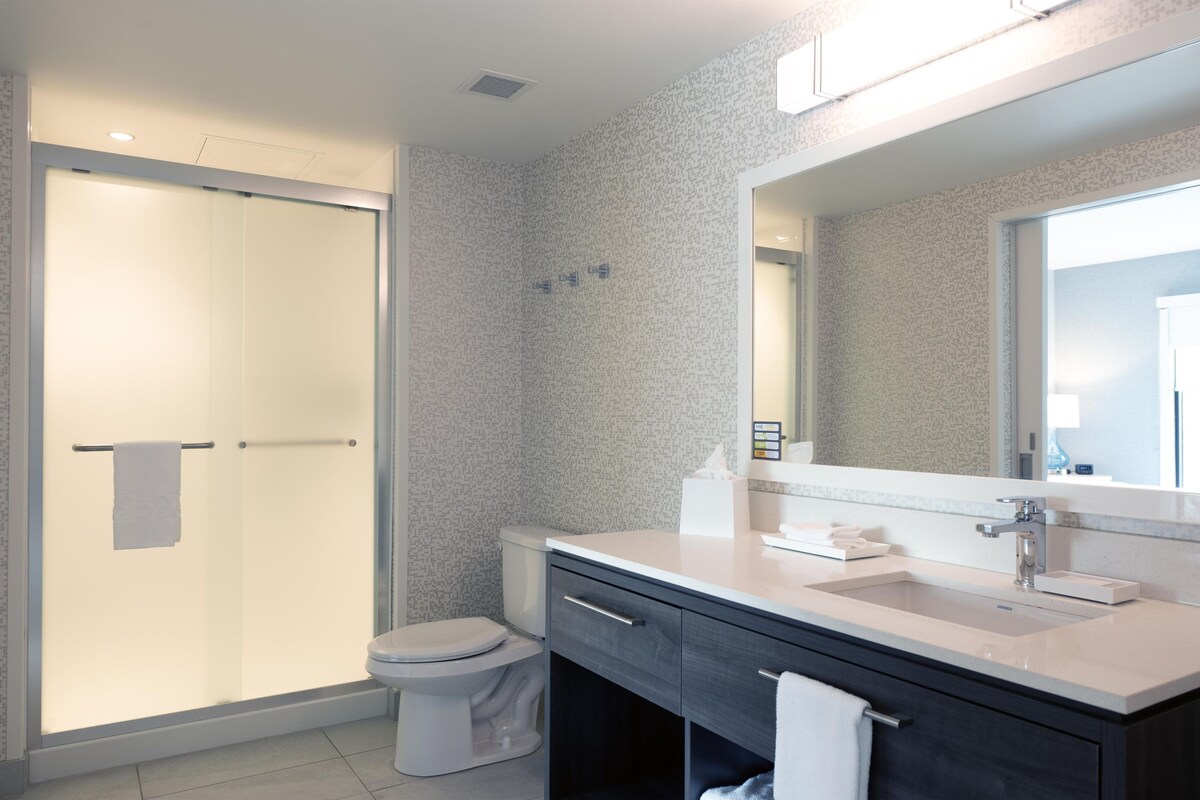 Une salle de bain moderne équipée d’une douche, de toilettes, d’un meuble-lavabo et d’un grand miroir.