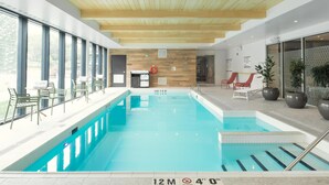 Una piscina interior con carriles delimitados, vigas de madera en el techo y zonas de estar con mesas y sillas.