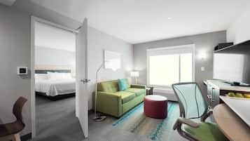 Quarto de hotel com cama, sofá verde, banquinho vermelho, escrivaninha com computador e televisão.