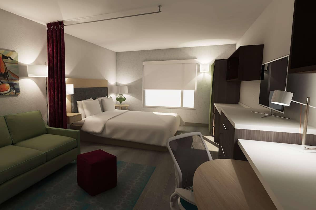 Een hotelkamer met een bed, een groene bank, een bureau, een televisie en een schilderij aan de muur.