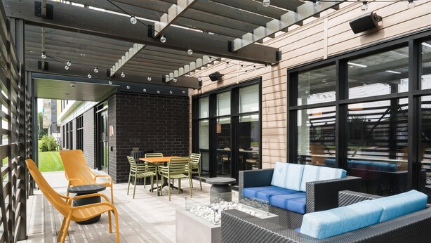 Un espacio al aire libre moderno con mobiliario de mimbre, una chimenea y ventanas amplias.