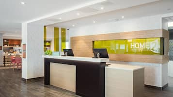 Ein Hotel-Empfangsbereich im modernen Design, mit einer Rezeption, einer Sitzgruppe mit Stühlen und einer im Hintergrund sichtbaren Küche.