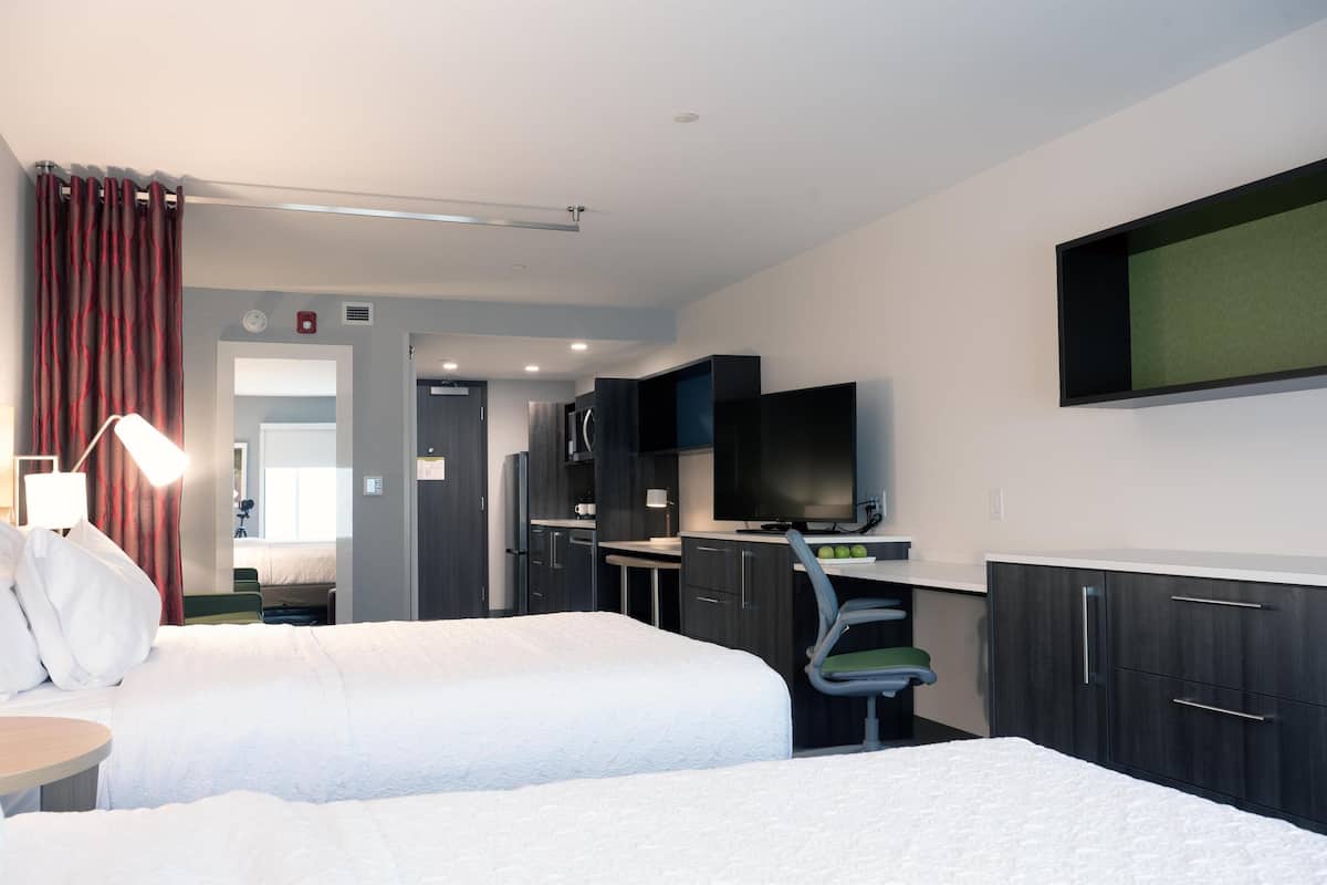 Een hotelkamer met twee bedden, een bureau met stoel, een televisie en een kitchenette.