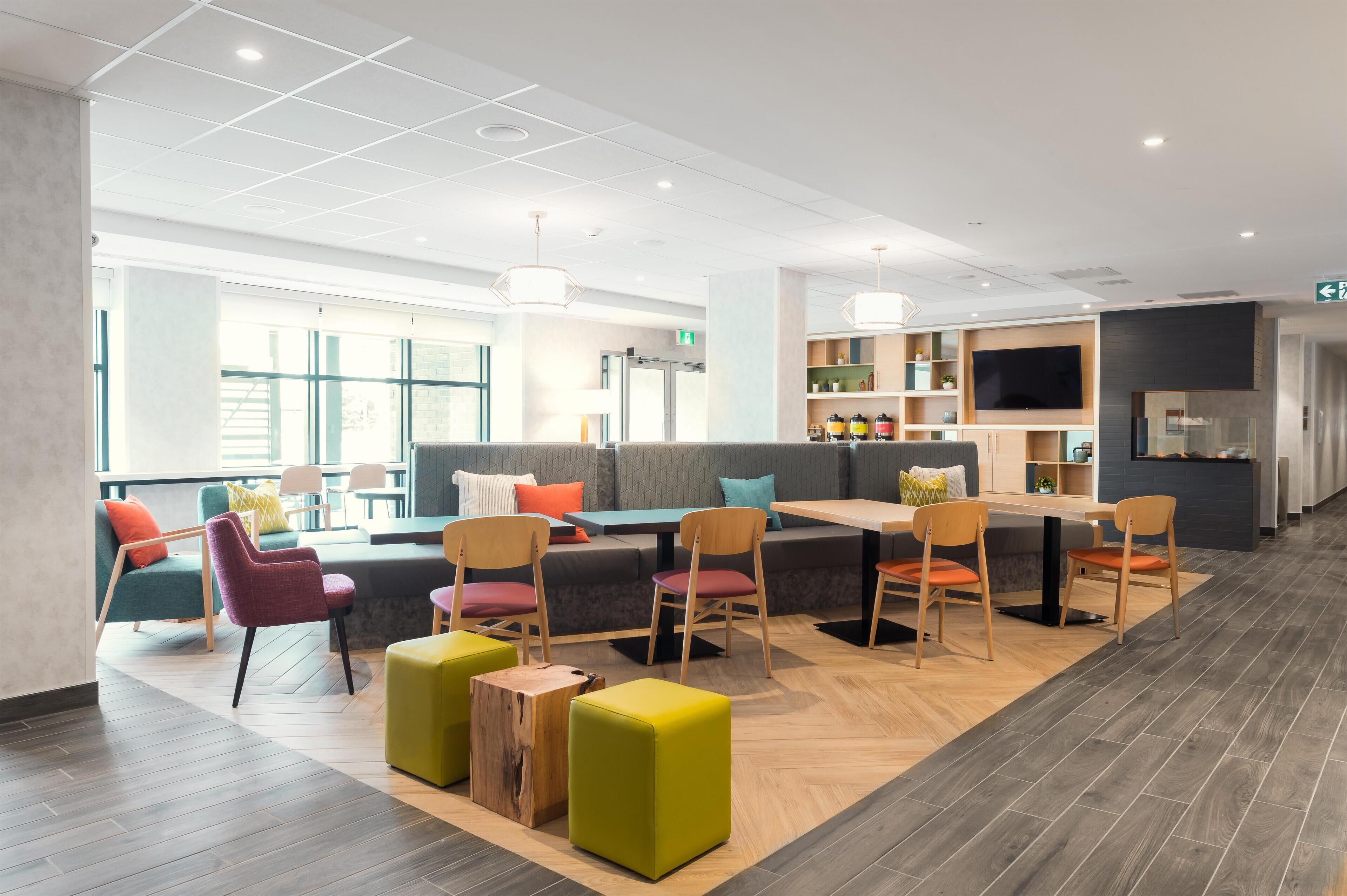 A modern hotel lobby with a seating area, a television, and a kitchen counter.
