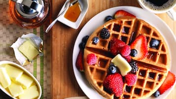 A waffle topped with strawberries, blueberries, and blackberries, accompanied by butter and syrup.