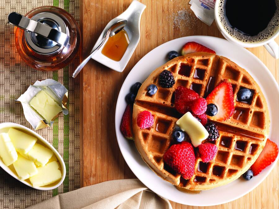 A waffle topped with strawberries, blueberries, and blackberries, accompanied by butter and syrup.