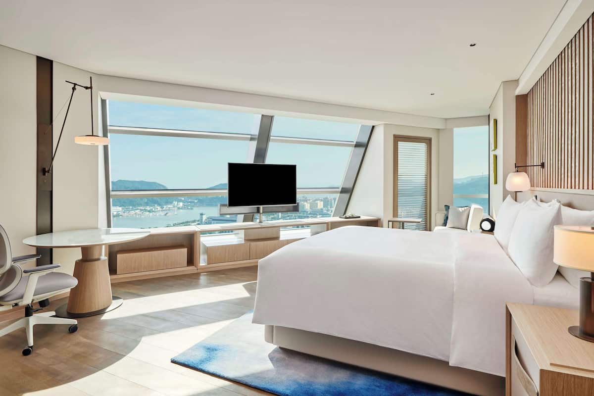 Habitación de hotel moderna con una cama grande, un escritorio, un televisor y vistas a la ciudad.