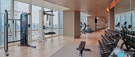 A modern gym with various exercise equipment, large windows, and a city view.