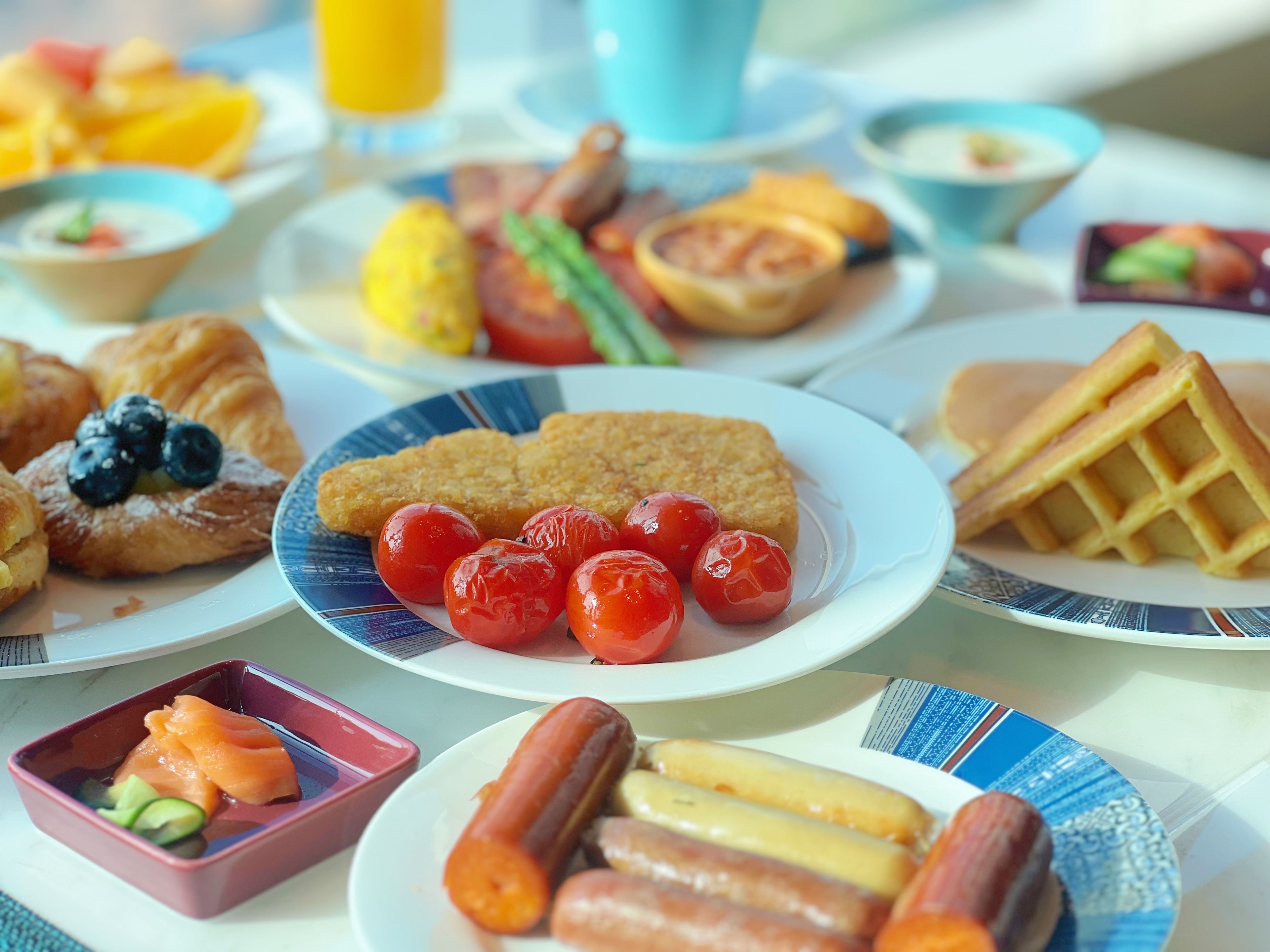 A breakfast table with various dishes including croissants, waffles, and sausages.