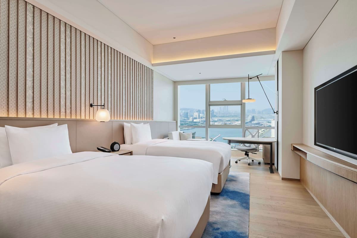 Habitación de hotel con dos camas, un escritorio, una silla, un televisor y vistas a la ciudad.