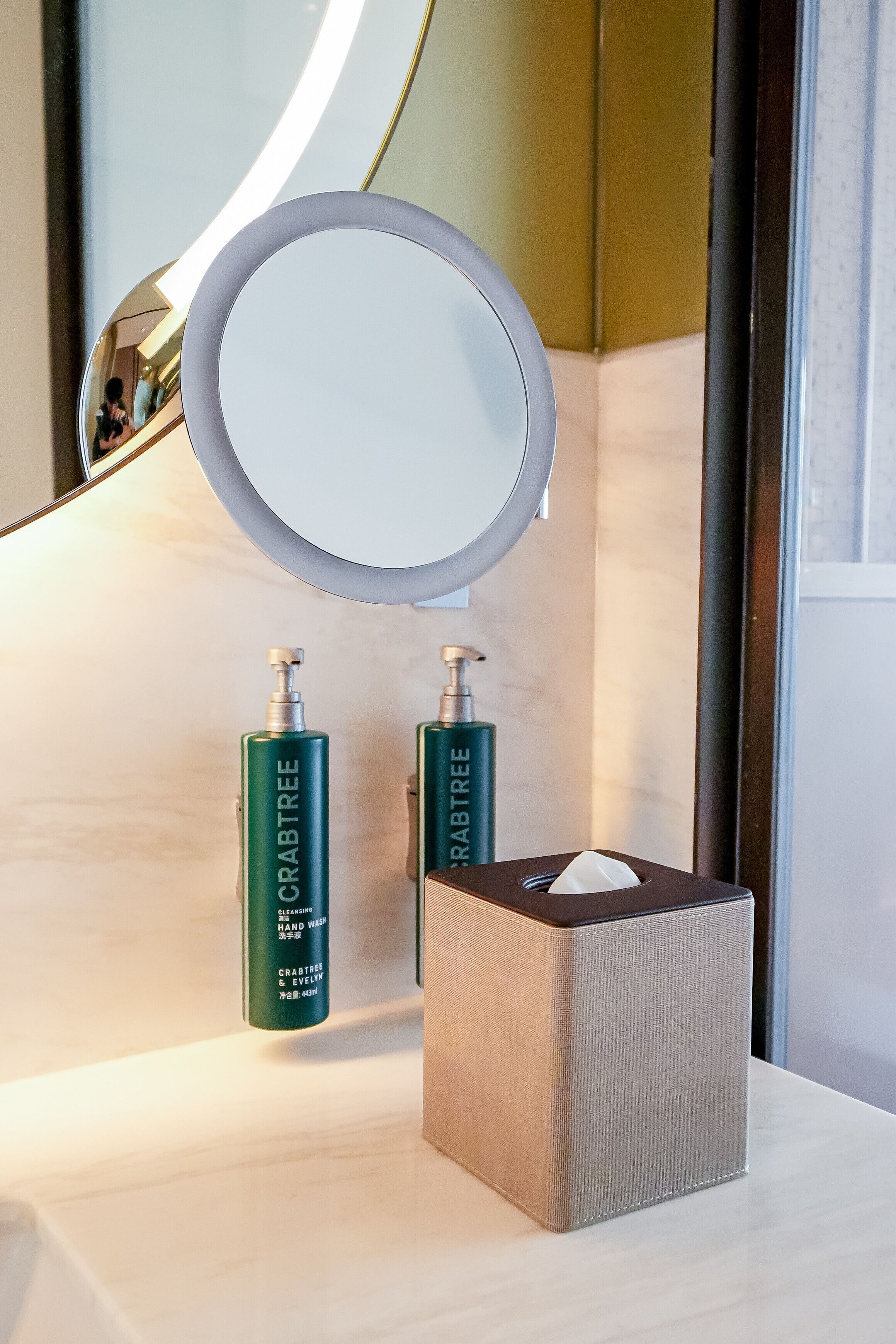 Un meuble-lavabo de salle de bain avec un miroir, deux flacons de savon liquide et une boîte de mouchoirs.