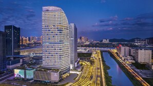 A modern hotel with a curved facade, located near a river with a highway and other buildings in the background. - Doubletree By Hilton Zhuhai Hengqin (Zhuhai)