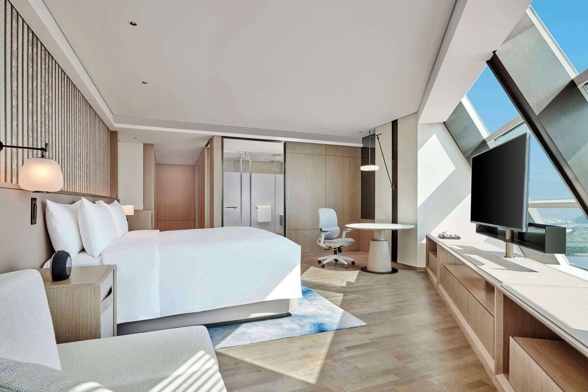 Una habitación de hotel moderna con una cama grande, un escritorio, una silla y un televisor.