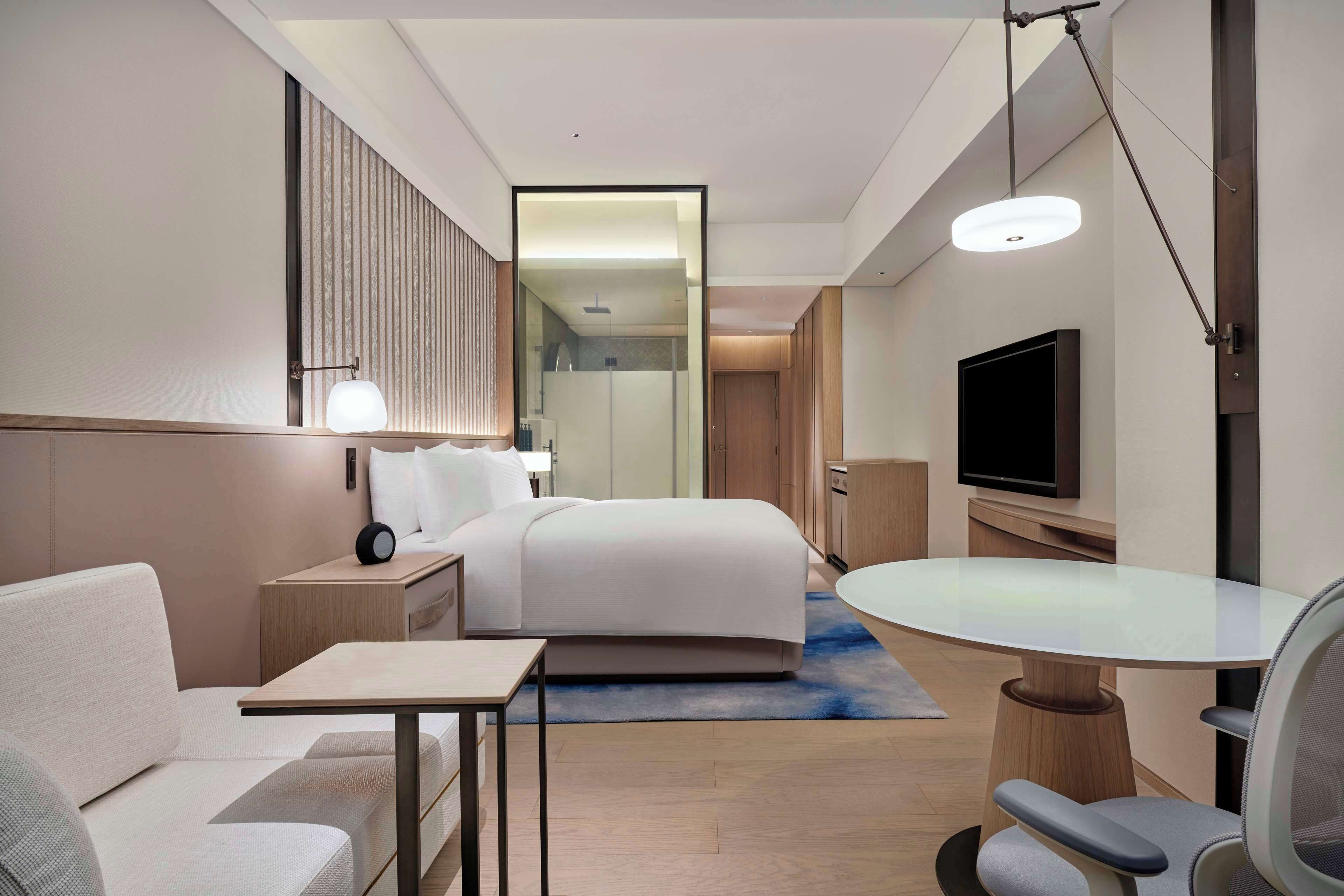 A modern hotel room with a bed, a desk, a chair, a TV, and a mirror.
