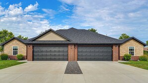 A two-story house with a garage, a driveway, and a well-maintained lawn. - Charming Ozark Abode w/ Yard & Pool Access (Ozark)