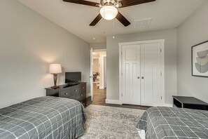 Une chambre avec deux lits, une commode, un téléviseur et un ventilateur de plafond.