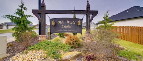 A sign for Olde' World Estates with a landscaped entrance featuring rocks, shrubs, and a wooden fence.