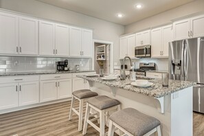 A modern kitchen with white cabinetry, a granite countertop, stainless steel appliances, and a bar stool seating area.