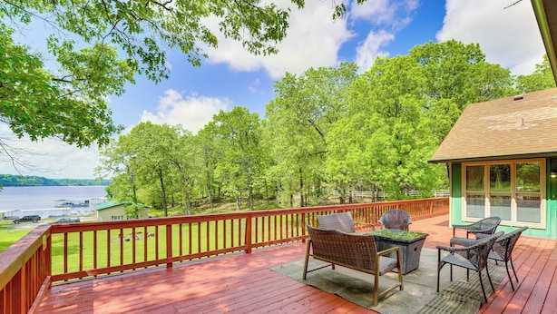 A wooden deck with outdoor furniture, a view of trees and a body of water. - Large Lakefront Home | Pool, Hot Tub & Boat Dock (Grove)
