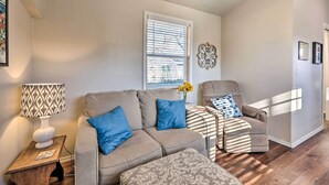 A living room with a sectional sofa, a patterned ottoman, a side table with a lamp, and a window with blinds. - 1 Mi to Dtwn Rogers: Convenient Getaway w/ Patio (Rogers)