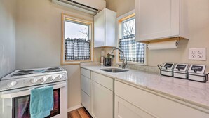 A compact kitchen with a stove, sink, and a window with checkered curtains. - 1 Mi to Dtwn Rogers: Convenient Getaway w/ Patio (Rogers)